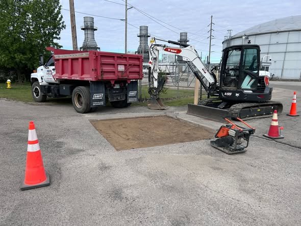Pavement cut out and base prepped at a power station with dump truck and Bobcat E55